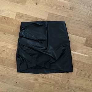 Kjol  - Tajtare kjol med drapering framtill, svårt att fota. I skinnimitation. Aldrig använd, lappen sitter kvar. Hund finns i hemmet 