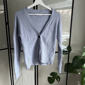 Kofta - En ljusblå ribbstickad kofta från Ellos i storlek 34/36. Koftan har tre knappar och är djupt skuren