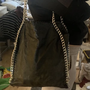 Svart väska med silver kedja - En jättefin och rymlig svart väska med silver kedja. Dragkedja på baksida. Säljer den då jag inte använder den. Den har ett litet hål på baksidan av väskan. Köpt för 550kr