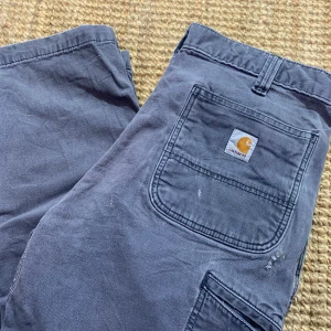 Carhartt byxor - Ett par feta Carhartt byxor. Dem har ett hål ovanför högra fickan och en röd fläck på vänster bakficka. Bara att skriva för fler bilder:)     Ytterben 104cm  Benöppning 21cm