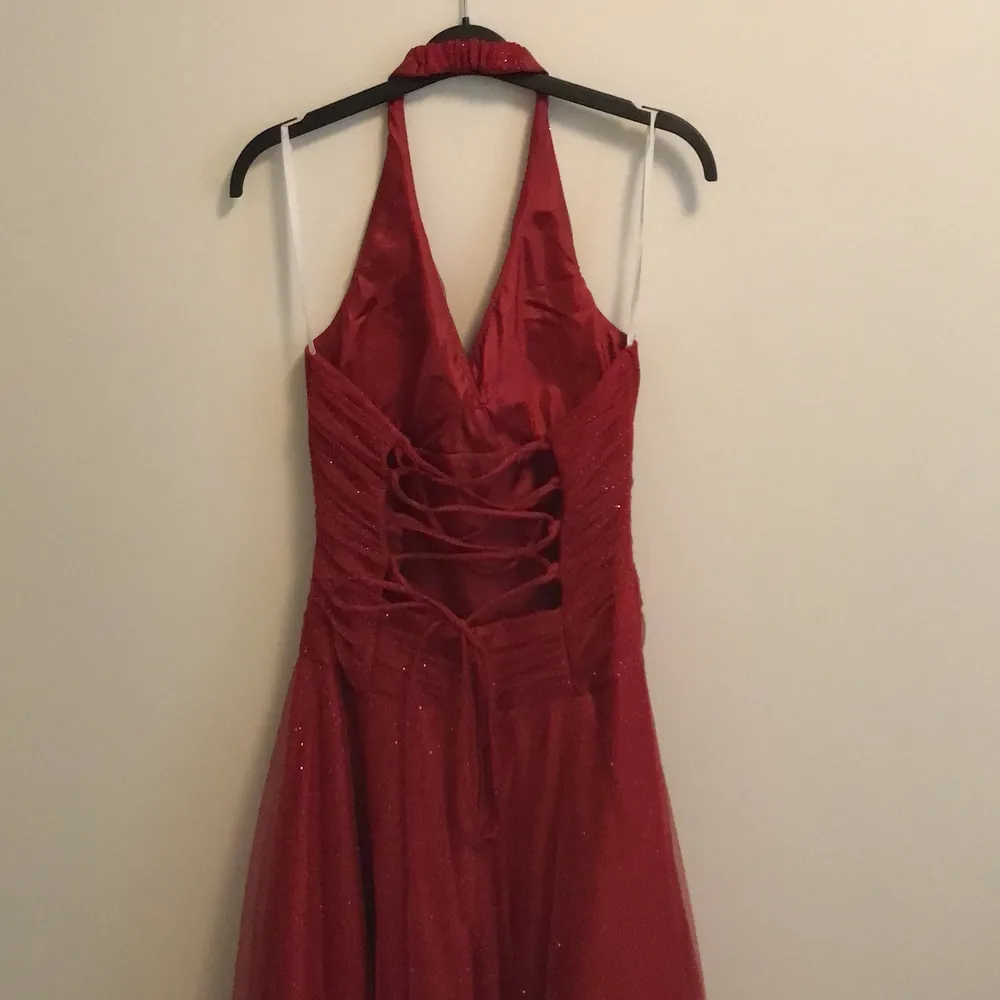 En lång röd balklänning. Klänningen är halterneck och glittrig. Med en fin knytning i ryggen. . Klänningar.
