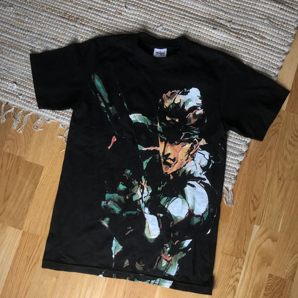 MGS-tisha med jumbotryck av Snake. Köpt från USA. Tror inte den går att få tag på längre då det var en pre-order som endast gjordes i få exemplar. Tishan är 6oz så väldigt tjock vilket ger en stabil vintage känsla. Sitter som en S/M. T-shirts.