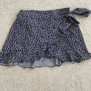 Kjol - Säljet denna blommiga kjolen då den inte kommer till använning. Den är i den kortare modellen. Men den är sjusterbar då det är en omlottkjol med band som man knyter. Frakt tillkommer