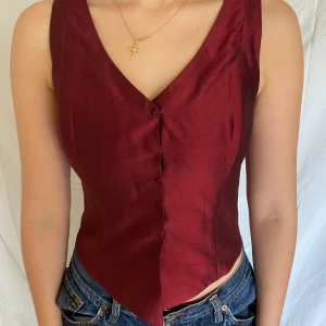 Väst/korsett  - En snygg väst som sitter bra på kroppen, lite byggt som en korsett som gör att båda alternativen funkar fint. Vinröd snygg färg. Rekommenderar inte personer med stor byst då knapparna kan lättare knäppas av