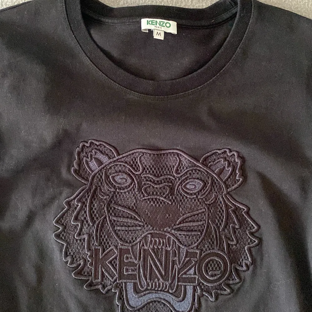T-shirt från Kenzo i boxig modell. Tröjan och märket är helsvart. Kraftig bomull i mycket bra kvalitet. Mycket gott skick, använd 1 gång, säljer pga lite för liten. Avklippt tvättetikett inne i tröjan pga skavde mot huden men självklart äkta Kenzo. . T-shirts.