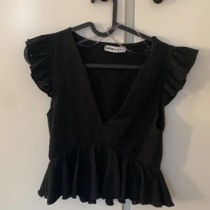 Topp  - Svart topp med volanger på ärmarna å nedre kanten 