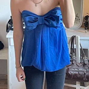 Kornblå klänning - En kort kornblå klänning utan band. De finns kardborre högst upp så klänningen fäster mot tex en bh. Finns resor längst ner som gör att den kan användas som både klänning eller top