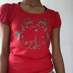 Snygg röd tröja - En röd tröja med texten ”BANANA FISH” samt med två katter. Tröjan är U ringad och har lite puffiga axlar.Baksidan av tröjan har också texten ” BANANA FISH”. Tröjan är lite sliten då några ”diamanter” har fallit av men det syns dock inte när man har på tröjan om man inte kollar noggrant. 