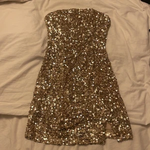 Glitter bandeu klänning - Säljer denna super festliga klänning då jag tänkte ha den på nyår men hittade en annan. Aldrig andvänd med lappen kvar. Är med guldiga paletter och super fin. Andra bilden fast i guld. Frakt tillkommer.