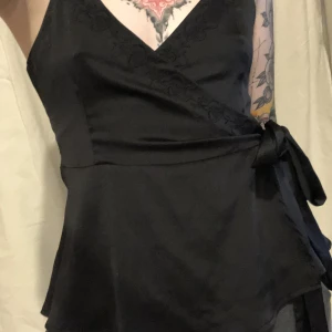 V-ringad satin topp - Vringad satin linne med brodyr runt halsen, omlott design med knytning på sidan , typ volang nertill, Ej använd