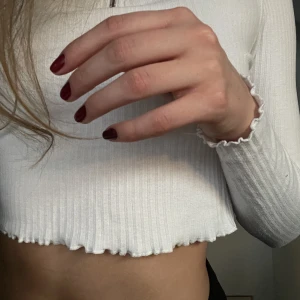 Långärma vit polo - En croppad långärmad vit ribbad polo med dragkedja med en ting på. Små ”ruffles” både längst ner på tröjan men även slutet på ärmarna:)