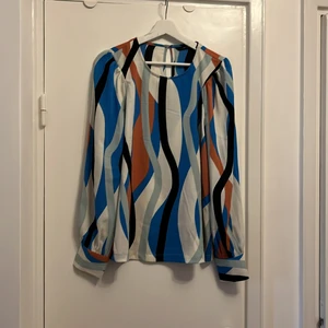 Färgglad blus från Vero Moda - Blus i svalt tyg, i färgerna vitt, orange, kornblå, mint och svart. Små tygklädda knappar i ärmslut och en i nacken. Lite krinklat tyg i axlarna som förstärker ballongarmarna. 