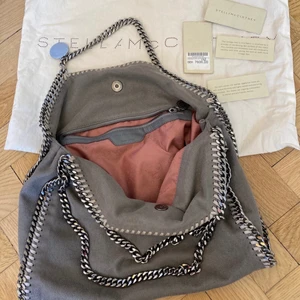 Väska  - Säljer min gråa Stella McCartney tote bag då den inte har använts så mycket som den förtjänar!   Dustbag ingår och certifikat finns. Köpt på Nathalie Schuterman, nypris 7600kr.   Sparsamt använd och i fint skick. Lite slitningar på läder, kedja och lite missfärgningar längs med kanten, se bilder.   Veganskt läder.   Höjd: 36cm  Bredd: 37cm