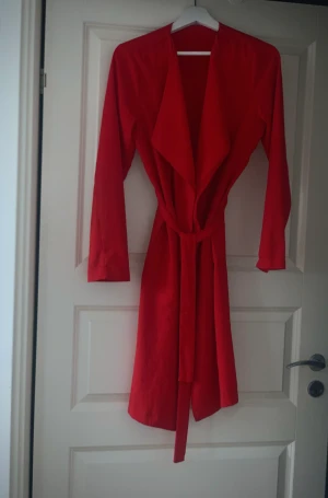 Röd tunnkappa, nyskick - Säljes en nyskick tunnkappa då den inte kommer till användning. En väldigt fin kappa som man kan använda till ett par ljus blå jeans etc.   Säljer för 280kr, först till kvarn! 