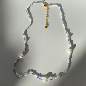 detta fina halsband är gjort av blåa, vita, guldiga samt randiga pärlor😍 halsbandet har även fejk sötvattenspärlor i olika storlekar😍✨ halsbandet passar till alla olika tillfällen✨ knutgömman, låset och kedjan är gulpläterade😍✨