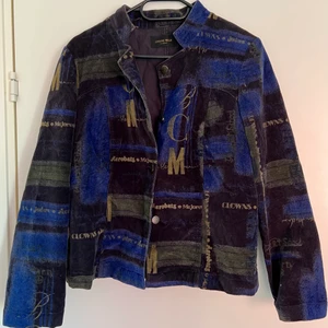 Skjortjacka med mönster  - En blå/svart/guld mönstrad Godske skjorta. Slutar vid höftbenen på mig som är 163 cm lång. Fina gulddetaljer i form av text runt hela jackan, och har en varierande mörkblå och svart färg. Jackan har axelvaddar som man kan klippa bort om man vill. Säljer pga flytt och utrensning av garderob. 