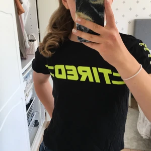 Topp med neondetaljer - Cool svart tröja i nyskick, textmotiv (Tired) och korsande band på ärmarna. Slutsåld, finns inte mer!