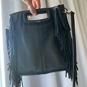 Maje väska  - Säljer min svarta skinnväska från Maje. Inköpt för ca 2500kr. Använd fåtal gånger. Till väskan ingår en silvrig kedja  samt det bandet som syns på bilden (pris för bandet ca 900kr ingår). Banden går att ta av om så önskas.