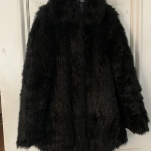 Längre fakepälsjacka - En längre jacka i fakepäls från H&M. Jackan knäpps med knappar, har fickor framtill och detaljer av mockaimitation på insidan av ärmarna.  Köpt för 699kr och använd ett fåtal gånger. Säljs för att den inte används.  Köparen står för frakt. 