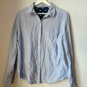 Skjorta blå & vitrandig - Blå & vitrandig skjorta från okänt märke. Pyjamasskjorta, men har inte använts som det. En udda knapp längst upp (den i guld), dock är det enligt original. Skjortan är använd,  men i mycket gott skick.