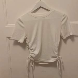 En helt vanlig vit t-shirt i ribbat med fina detaljer på sidorna som man kan justera hur kort eller lång tröjan ska vara.