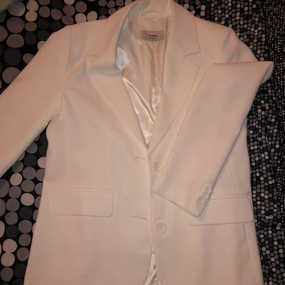 En blazer i vit/krämvit färg med knappar framtill och längst ärmarna. . Kostymer.