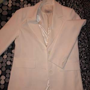 En blazer i vit/krämvit färg med knappar framtill och längst ärmarna. 