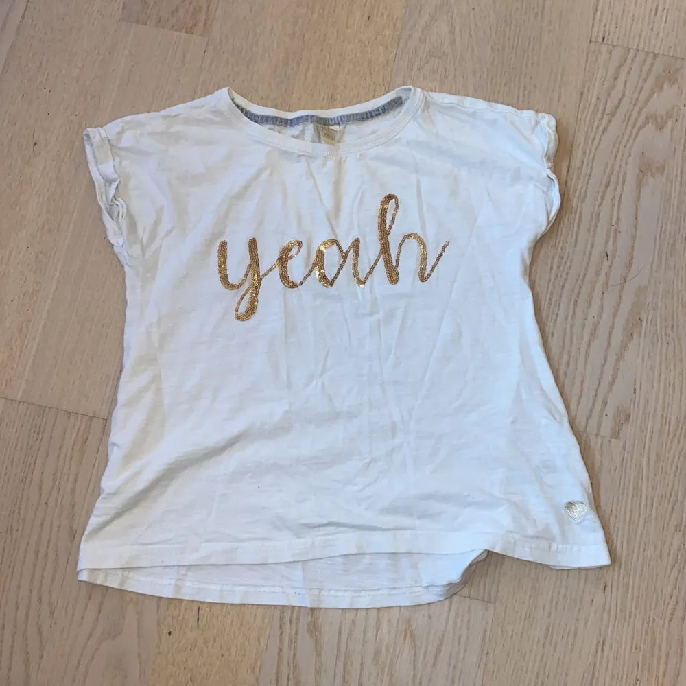 Jag säljer denna vita t-shirten med guldig text där det står  ”yeah”, storlek: 140. T-shirts.