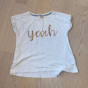 Jag säljer denna vita t-shirten med guldig text där det står  ”yeah”, storlek: 140