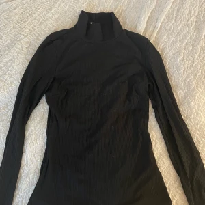 Svart polo - Svart ribbad polotröja. Inte så tjockt material men absolut inte genomskinlig. Från Nelly. Knappt använd. Normal i storleken, lite stretch