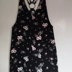 Hängslekjol i storlek 38 - En blommig hängselkjol med en liten ficka framtill. Har aldrig blivit använd, är helt ny! 
