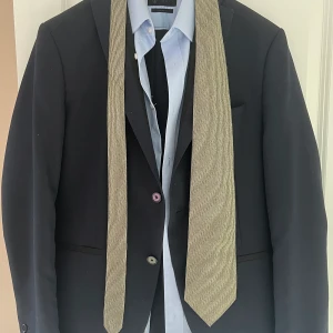 Hel kostym  - Säljer en hel kostym med byxor, kavaj, skjorta och slips. Färgen på kostymen är mörkblå, skjortan är ljusblå och slipsen är grön med svarta ränder. Storlek på kavajen är 50, byxorna är 44, skjortan är M. Kostymen är köpt från Zara. 