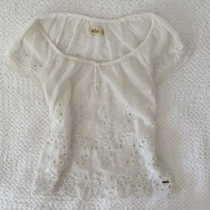 Vit blus - Säljer denna vita lite genomskinliga top med lite ihåliga blomdetaljer! Den kommer från Hollister och är i storlek S och i superbra skick! 