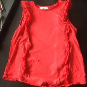 A red no sleeve shirt with a tie at the bottom. A puffy design that goes along the shoulders and all the way down for both sides (back and front).