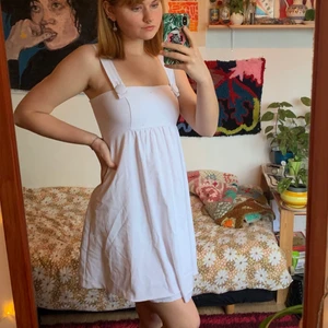 Vit klänning - Fin klänning helt i vitt, med knappar som håller fast axelbanden. Dragkedja i ryggen. Fållen har släppt framtill, men det går lätt att fixa med ett par stygn. Klänningen har två lager.