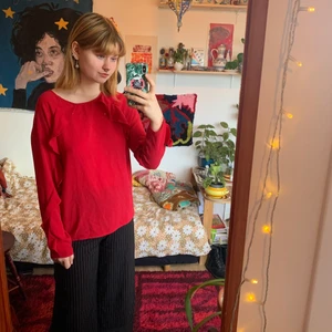 Röd blus med volanger - Klarröd blus med volanger som går hela vägen ner på ärmarna. Något stor i storleken. Knäppning i nacken (se bild)