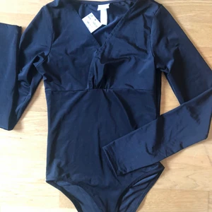 Body - Säljer denna bodyn från H&M i storlek xs. Är i ett glansigt material med en omlott detalj uppe. Den är helt ny med prislappen kvar på. Nypris 149kr.                     Köparen står för frakten!