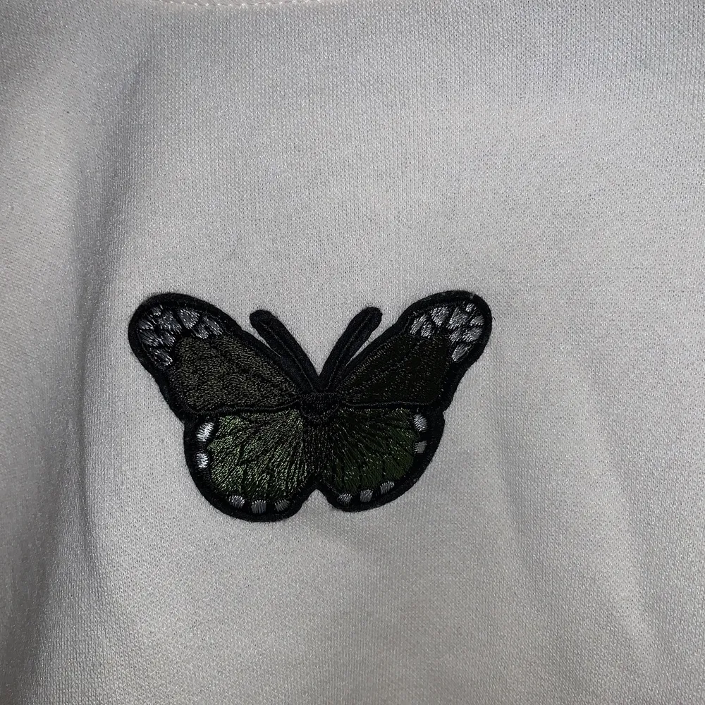 Beige croptop med en grön fjäril. Broderiet har jag fäst själv men tröjan är från HM. Offwhite/beige färg (ej vit). Neuletakit & Villapaidat.