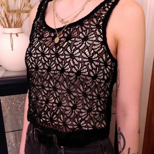 Svart tank-top i hålspets - Genomskinlig top med spindelvävsliknande mönster i tyget. Perfekt för den kommande sommaren. I med den löst sittande passformen så passar den perfekt för layering.