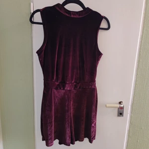 Shortsdress med öppen rygg i sammet - Shortsdress med öppen rygg, lila sammet. Använd en gång, superfin! Dragkedja bak, rosetten går att knyta upp så den är lätt att komma i. Stretchigt tyg, mjuk och skön