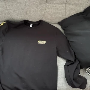 Moschino tröja  - Det är då en svart Moschino tröja me guldiga detaljer som är använd väldigt lite. Köpt i somras från Farfetch för 2085kr En väldigt snygg tröja säljs för att den är för stor för mig Kvitto finns  Intill nyskick  Pris kan sänkas vid snabb och bra affär  Storlek M