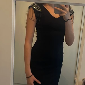 Svart klänning med silvriga detaljer  - Säljer en helt ny klänning från märket Zoul i storlek XS, prislappen är kvar, mitt pris är 240 kr och köparen står för frakten! Klänningen har silvriga och guldiga detaljer vid axlarna och det finns en dragkedja på baksidan.☺️
