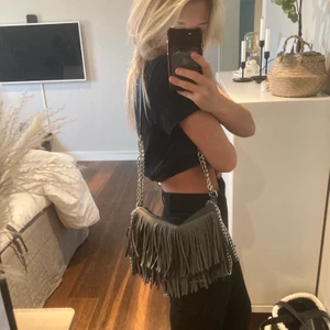 Frans väska - Denna väskan är allt. Galet snyggt det gråa hållet. Väskan är i jätte bra skick och bra kvalite med alla fransar kvar. Stängs med två magneter och en dragkedja och är mycket rymlig. Fallet så snyggt när man har den på axeln. Finns ett innerfack som stängs med ficka och sedan två innerfickor. 