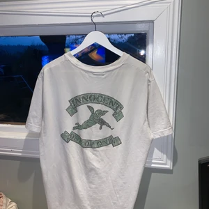 One of one i M - One of one INNOCENT t-shirt köpt på ett event i Visby, köpt för 500kr, grön INNOCENT logga på baksidan som blänker i solljus, medans framsidan är basic vit. Fler bilder kan skickas och köparen står för frakten