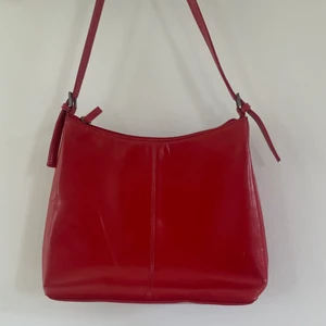 Röd handväksa - Röd handväska med funktionella fack i. Mått: 22cm hög, 27cm bred, 8cm djup. Justerbart axelband🌟