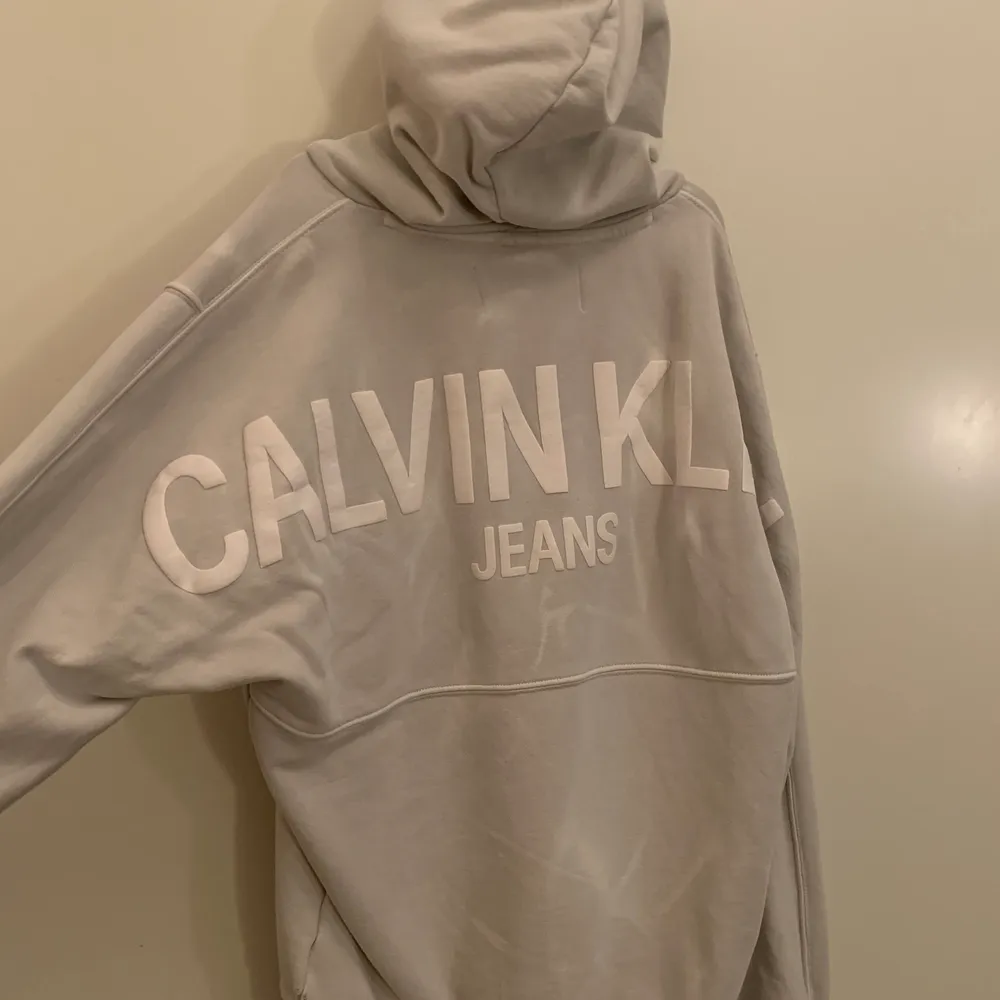 En Calvin klein hoodie i storlek M med ett tryck på ryggen. Den är i färgen grå och är lite vitspräcklig så den får en snygg marmor effekt. Hoodies.
