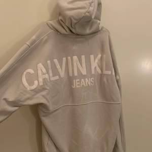 En Calvin klein hoodie i storlek M med ett tryck på ryggen. Den är i färgen grå och är lite vitspräcklig så den får en snygg marmor effekt