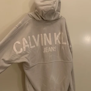 Calvin Klein Hoodie - En Calvin klein hoodie i storlek M med ett tryck på ryggen. Den är i färgen grå och är lite vitspräcklig så den får en snygg marmor effekt