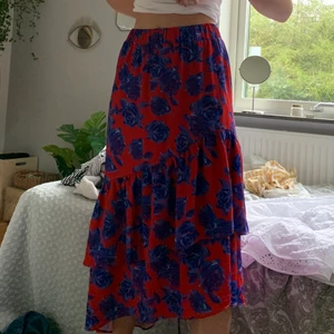 Kjol från NAKED  - Röd kjol med blåa blommor på, volanger så går snett ned mot fötterna