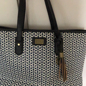 Blå mönstrad handväska - Blå mönstrad väska från märket Pipol’s Bazaar. Trasigt vid axelbanden, se bild 3 annars i gått skick. 3 små fack inne i väskan. Katt finns i hemmet.